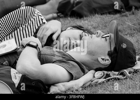 JUNGES PAAR SCHLAFT ZUSAMMEN, REPORTAGE, GREEN MAN FESTIVAL 2016, BRECON, WALES, UK, 2016: Ein junges Paar in Monochromie schläft friedlich zusammen auf dem Gras, die Hand der Frau ruht auf der Brust des Mannes. Foto: Rob Watkins. INFO: Das Green Man Festival begann 2003 in Wales. Jährlich findet es am dritten Wochenende im August in den Brecon Beacons statt und feiert alternative Musik, Kunst, Literatur, Wissenschaft und familienfreundliche Kultur in einer wunderschönen Berglandschaft. Stockfoto
