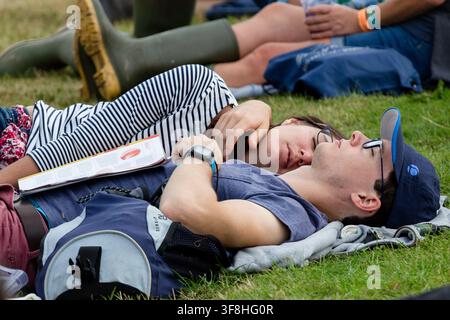 MÜDE PAAR RUHT SICH AUF EINEM FESTIVAL AUS, REPORTAGES, GREEN MAN FESTIVAL 2016, BRECON, WALES, UK, 2016: Ein junges Paar mit Brille, einer trägt ein gestreiftes Oberteil, schläft zusammen auf dem Rasen mit einem offenen Buch neben ihnen. Foto: Rob Watkins. INFO: Das Green Man Festival begann 2003 in Wales. Es findet jährlich am dritten Wochenende im August in den Brecon Beacons statt und feiert alternative Musik, Kunst, Literatur, Wissenschaft und familienfreundliche Kultur in einer wunderschönen Bergkulisse. Stockfoto