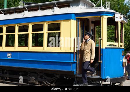 Straßenbahnführer in Vintage-Uniform gähnt, als er aus der historischen blauen Straßenbahn Nr. 196 am Beamish Living Museum of the North, UK, steigt. Stockfoto
