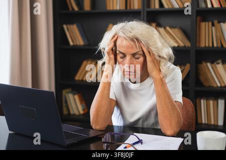 Kopfschmerzen. Frau mittleren Alters, die Schläfe berührt und Stress erlebt. Reife alte Dame müde der Arbeit, Kopfschmerzen krank, die Schläfen an der Stirn reibt. Long-Laptop-Nutzung Computer Vision Office Syndrom Stockfoto