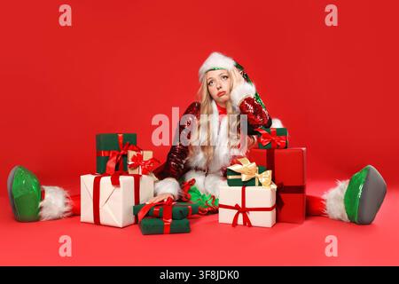 Frau in Elfenkostüm mit Weihnachtsgeschenken auf rotem Hintergrund Stockfoto