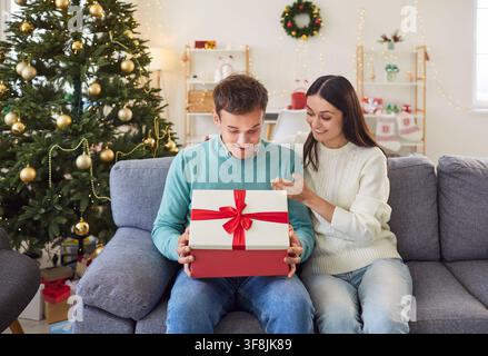 Junger Mann öffnet eifrig ein Weihnachtsgeschenk und schaut mit aufrichtiger Bewunderung in die Schachtel. Stockfoto