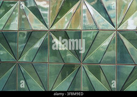 Ansicht von geometrischen grünen Keramikfliesen mit einem facettierten dreieckigen Muster an einer Wand in London, England, Vereinigtes Königreich. Stockfoto