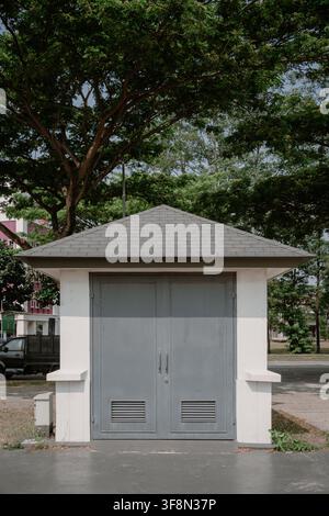 Kleines Nebengebäude mit grauen Doppeltüren und dunklem Schindeldach, umgeben von Bäumen in einem öffentlichen Parkbereich. Stockfoto