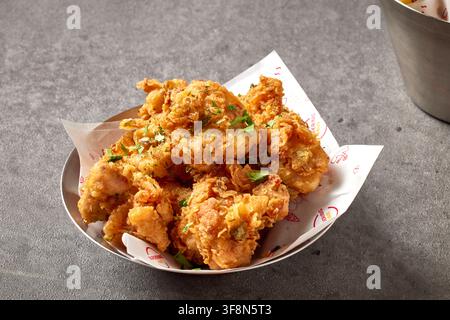 Knuspriges frittiertes Hühnerpopcorn und Calamariringe, serviert in einem Korb und auf einem schwarzen Tablett mit Dipsauce auf einem rustikalen Holzuntergrund, Restaura Stockfoto