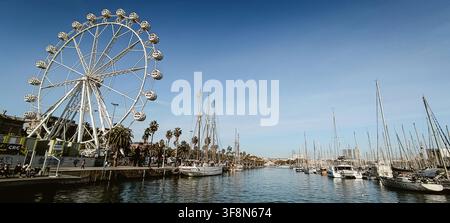 Barcelona, Spanien - 05. Dezember 2025: Blick auf das Riesenrad am Port Vell mit Segelbooten, die im Hafen vor Anker liegen, unter einem klaren blauen Himmel. Stockfoto
