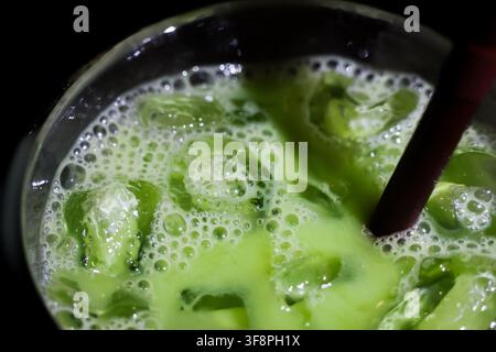 Ein cremiges, geeistes Matcha-Latte mit Schaum aus grünem Tee, Eiswürfeln und Strohhalm, ein erfrischendes kaltes Getränk, das an einem warmen Tag als süße Stärkung genossen wird Stockfoto