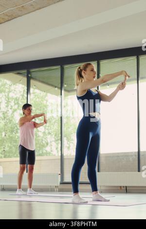 Vertikales Bild einer kaukasischen jungen Frau und einer reifen Frau, die sich im Fitnessstudio die Hände reichen, und das Wohlbefinden und einen gesunden Lebensstil fördert, ideal für Fitnessstudio-Marketing Stockfoto
