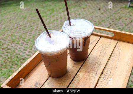 Ein Eiskaffee-Getränk mit Schaum und Schokoladendrizzle in klaren Plastikbechern auf einem Holztray, einladende entspannte Erfrischung im Freien und lässiger Sommergenuss Stockfoto