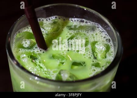 Ein Eismatcha-Latte mit Milch und Eiswürfeln im Glas, erfrischendes grünes Tee-Getränk mit Strohhalm und Schaum Stockfoto