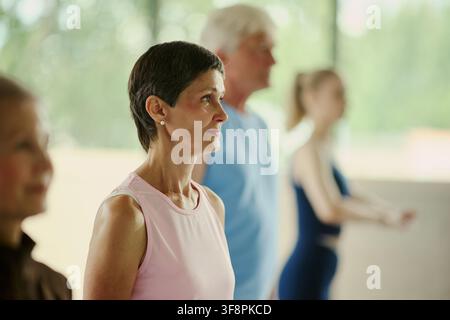 Reife kaukasische Frau nimmt an einer Gruppengymnastikstunde mit einem Senior und einer jungen Frau teil, fördert einen aktiven Lebensstil und Wohlbefinden, Mittelformat Stockfoto