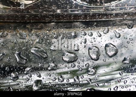 Ein Regentropfen auf einer Metalloberfläche mit reflektierenden Wassertröpfchen, die eine abstrakte Textur und stimmungsvolle Atmosphäre erzeugen Stockfoto