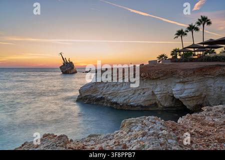 Sonnenuntergang über der Küste von Zypern, mit einem Schiffswrack vor der Küste, Kalksteinklippen und Palmen, die das Mittelmeer überblicken. Stockfoto