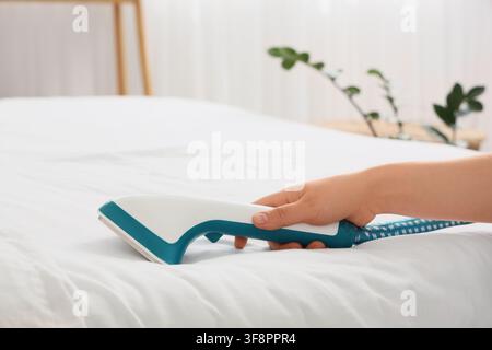 Hand, die einen modernen Stoffrasierer hält, der Flusen von weißen Bettlaken entfernt, Haushaltsarbeiten und Textilpflege Stockfoto
