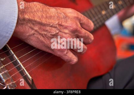 Männerhand zupft Nylonsaiten auf einer roten Akustikgitarre während eines Auftritts Stockfoto