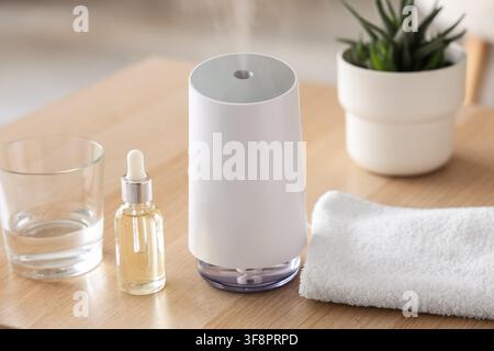 Moderner weißer ätherisches Öle-Diffusor mit Dampf, Aromatherapie- und Wellnessprodukten auf einem hellen Holztisch Stockfoto