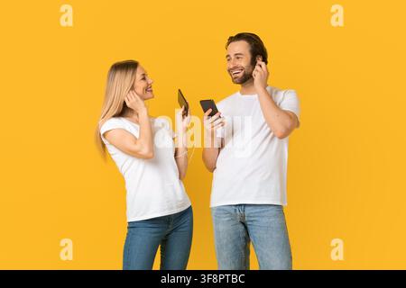 Glückliches junges Paar, das zusammen Musik hört, lächelnd, gelber Hintergrund Stockfoto