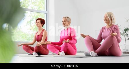 Drei lächelnde reife Frauen praktizieren Yoga und Meditation in einem hellen Studio und fördern gesunde Alterung und Wohlbefinden Stockfoto