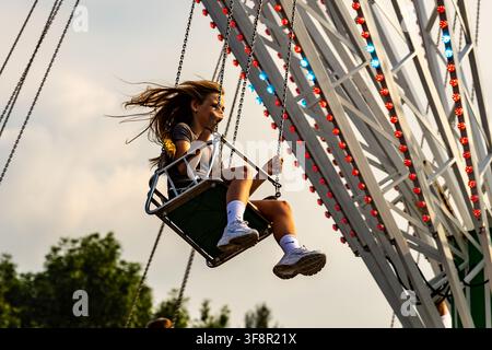 Junge Frau genießt eine Karussellfahrt auf dem Sommerfest Stockfoto