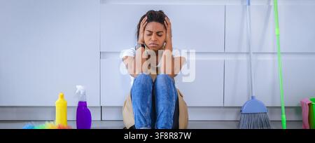 Besorgte schwarze Reinigungskraft, die im Innenbereich Stress beim Putzen erlebt Stockfoto