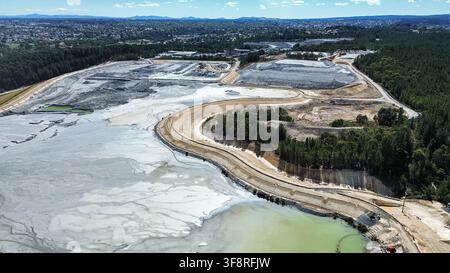 Luftaufnahme einer Bergbaustätte mit Tailings-Teich und Erdbewegungen in der Nähe eines urbanen Gebiets, die die Umweltbelastung zeigen Stockfoto