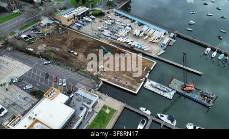 Luftbild zeigt die Sanierung einer Marina mit Erdbewegungsgeräten, Neubauten, geparkten Booten und einem Schwimmkran im Wasser Stockfoto