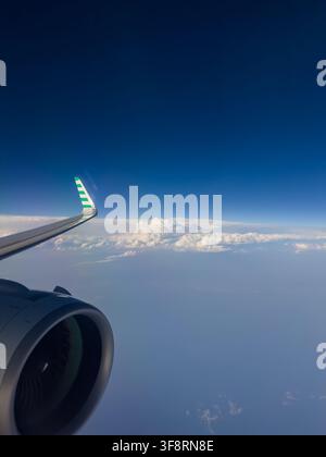 Blick aus dem Flugzeugfenster, der ein Triebwerk und einen Flügel über einem weiten blauen Ozean und einer Wolkenschicht zeigt Stockfoto