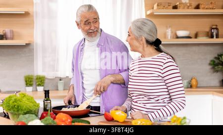 Glückliches älteres kaukasisches Paar kocht zusammen in der Küche und genießt die gemeinsame Zeit Stockfoto