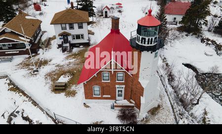 Luftaufnahme des historischen Eagle-Harbor-Leuchtturms mit seinem markanten roten Dach, umgeben von schneebedeckten Grundstücken und Gebäuden in Eagle Harbor, Mi Stockfoto