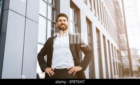 Selbstbewusster kaukasischer Mann im Geschäftsanzug vor einem modernen Bürogebäude, Geschäftskonzept Stockfoto