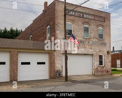 Liberty, NC, USA – August 2026: Ehemaliges Fabrikgebäude der Liberty Broom Works mit verwitterter Ziegelverkleidung und historischer Beschriftung. Stockfoto