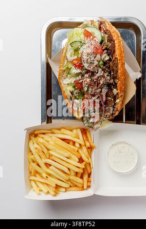 Doner-Kapsandwich in Sesambrötchen mit Pommes und Soße auf dem Tablett Stockfoto