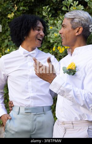 Zwei afroamerikanische Männer, die im Garten lächeln und sich unterhalten, mit Fliege und gelbem Rosen-Boutonniere Stockfoto