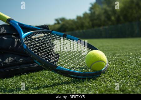 Nahaufnahme eines Tennisschlägers und eines gelben Balls, die auf einem grünen Rasenplatz im Sommersonnenlicht liegen, Outdoor-Sport- und Trainingskonzept mit Kopierraum. Stockfoto