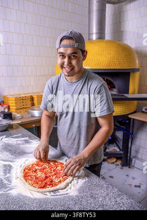 Koch macht Pizza mit seinen Händen und legt die Zutaten für die Pizza auf den Tisch. Mannkoch bereitet eine Pizza in einer italienischen Restaurant-Pizzeria vor. Essen Stockfoto