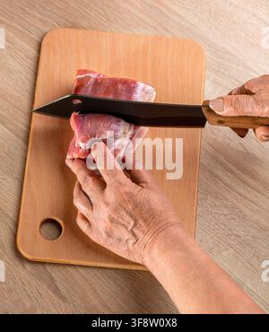 Männerkoch schneidet Schweinefleisch mit einem Messer in einem Restaurant. Fleisch schneiden. Metzger schneidet das rohe frische Schweinefleisch auf einer Holzplatte. Stockfoto