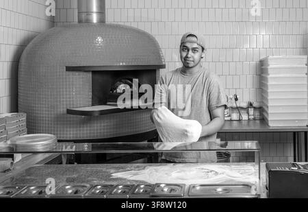 Teig für Pizza, der mit den Händen gerollt wird, während man in einer Pizzeria arbeitet. Der Prozess der Herstellung von Pizzen. Schwarzweiß Stockfoto