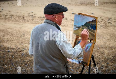Künstler malt eine Meereslandschaft en plein air auf einer tragbaren Staffelei am Strand von Southwold mit Küstenstrandhütten, Suffolk, England, UK. Stockfoto
