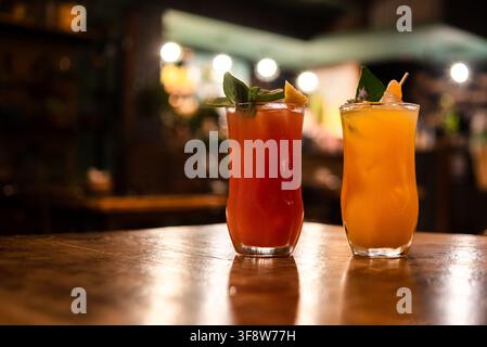 Zwei farbenfrohe tropische Cocktails mit Garnitur auf einer hölzernen Theke mit unscharfen Hintergrundlichtern Stockfoto