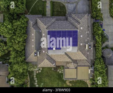 Luftbild von Photovoltaikanlagen und Solarpanelen auf einem Wohngeschäftsgebäude, umgeben von üppigen grünen Bäumen und einem gepflegten Hinterhof Stockfoto