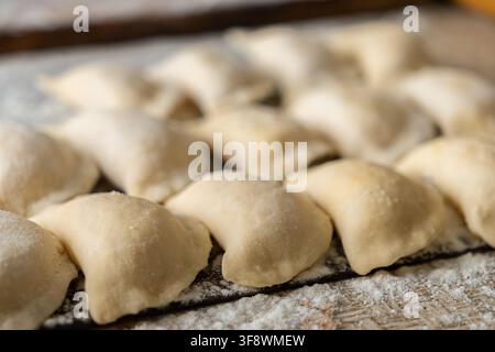 Ungekochte Knödel warten auf einer bemehlten Oberfläche und heben den Prozess der hausgemachten Teigzubereitung für authentische Mahlzeiten in einer gemütlichen kulinarischen Umgebung hervor fo Stockfoto