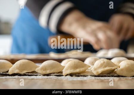 Rohe Teigtaschen ordentlich auf einer Küchentheke angeordnet, während ein Bäcker mit einer Teigrolle authentische Mahlzeiten herstellt, was die Kunst des Profis repräsentiert Stockfoto