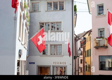 Schweizer Flaggen, die an historischen Gebäudefassaden in der Strehlgasse Altstadtmauer hängen. Zürich, Schweiz - 23. Juni 2026. Stockfoto