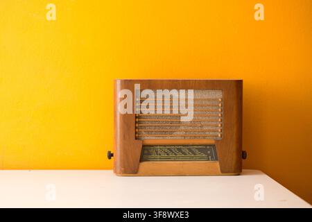 Vintage-Holzradio auf einem weißen Tisch vor einem hellgelben Wandhintergrund Stockfoto