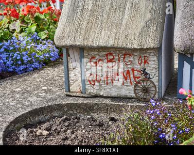 Miniatur-Steinhaus im Merrivale Model Village, Great Yarmouth, mit rotem Graffiti-Text 'GO BIG OR GO HOME' und einem Banksy-Ratten-Schablonenbild. August Stockfoto