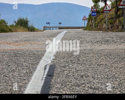 Eine kurvenreiche Asphaltstraße erstreckt sich vor uns mit einem steilen Abhang auf der rechten Seite. Warnschilder weisen auf scharfe Kurven und eine Geschwindigkeitsbegrenzung von 40 hin. Die Szene Stockfoto