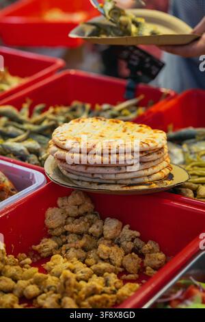 Gegrilltes Fladenbrot an einem Meeresfrüchte-Buffet mit einem Kunden, der Essen serviert. Ein Stapel gegrillten Fladenbrots wird an einem Meeresfrüchte-Buffet präsentiert, während ein Kunde Essen serviert Stockfoto