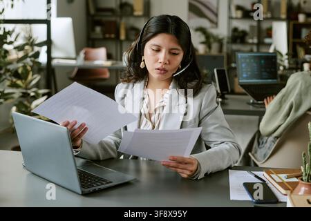 Hispanische Frau arbeitet in einem Callcenter und liest Dokumente Stockfoto