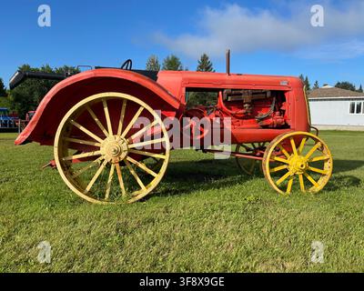 Ein klassischer roter Traktor von 1938 mit großen gelben Stahlrädern auf grünem Gras unter blauem Himmel, Plaisance, Quebec, Kanada Stockfoto