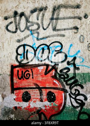 Nahaufnahme eines farbenfrohen Graffiti-Charakters, der auf einer verwitterten Betonwand mit Tags und Sprühfarben-Texturen gemalt ist Stockfoto